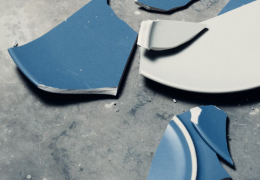 Shards of a broken blue and white ceramic plate scattered on a grey concrete surface.