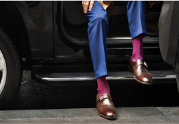 Lower body view of person wearing a blue suit and bright pink patterned socks stepping out of a black vehicle.