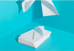A stack of white paper with a single pencil on top set against a vibrant bright blue background with floating paper sheets.